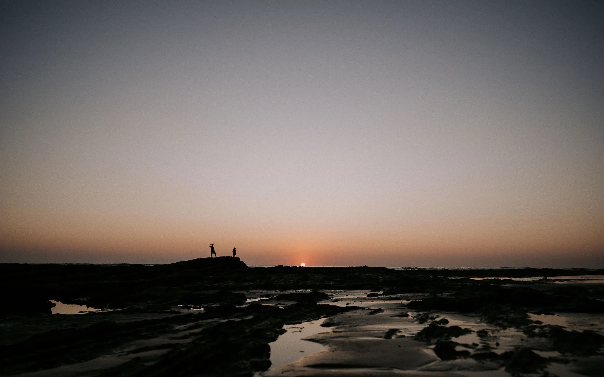Two people watching the sunset from the tidal rocks